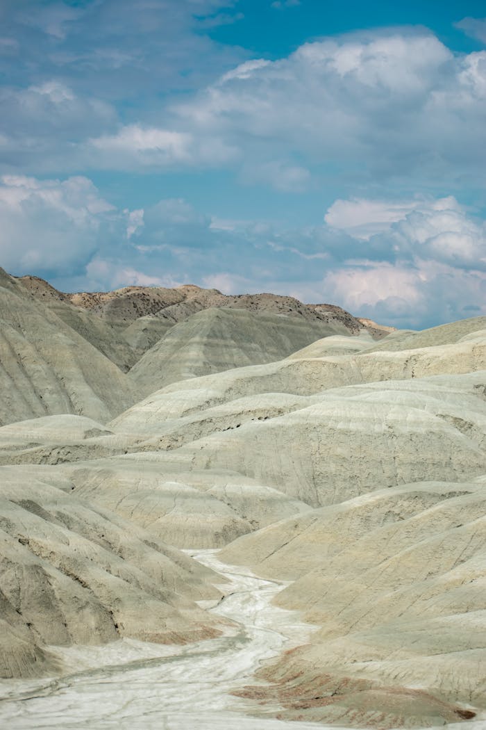 gallery-5 Stunning view of eroded hills under a vibrant blue sky with clouds.